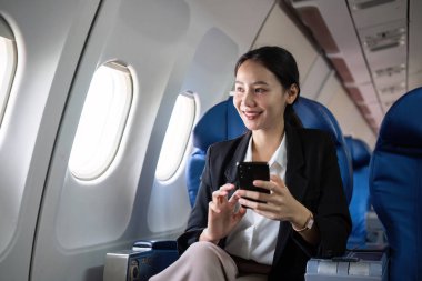 Genç muhasebeci bir uçakta çalışıyor, akıllı telefon ve dizüstü bilgisayar kullanıyor. Uçuş sırasında çalışan profesyonel bir iş kadını..