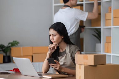 Bir çift, kutularla çevrili küçük online işlerini yürütmek ve bir ev ofisinde dizüstü bilgisayar ve akıllı telefon üzerinde çalışmak gibi sorunlarla karşı karşıya..