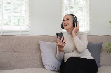 Yaşlı bir kadın rahat bir oturma odasında kulaklıkla müzik dinlemekten zevk alır..
