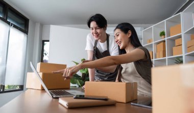 A couple collaborates in their home office, managing their online business with a laptop and packaging boxes. clipart