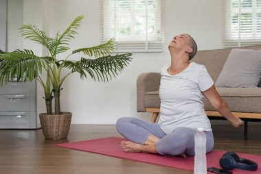 Parlak bir oturma odasındaki kırmızı paspasın üzerinde yoga yapan yaşlı bir kadın sağlığını, sağlığını ve aktif yaşam tarzını gösteriyor..