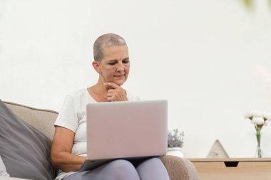 Yaşlı bir kadın rahat bir şekilde kanepeye oturur, rahat ve modern bir ev ortamında dizüstü bilgisayarıyla meşgul olur..