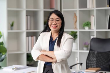 Kendine güvenen bir iş kadını modern bir ofiste duruyor, kollarını kavuşturup gülümsüyor, profesyonellik ve başarı yayıyor..