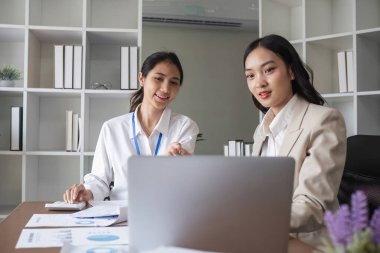 Modern ofis ortamında birlikte çalışan iki genç kadın muhasebeci takım çalışması ve profesyonelliği gözler önüne seriyor..