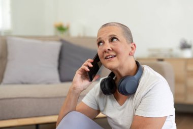 Yaşlı bir kadın, evde yoga yaparken akıllı telefonunu kullanarak modern teknolojinin ve sağlıklı bir yaşam tarzının karışımını sergiliyor..