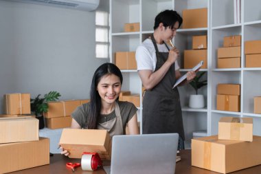 Ev ofisinde birlikte çalışan genç bir çift kutular dolusu mal paketliyor ve çevrimiçi satış yönetiyor..