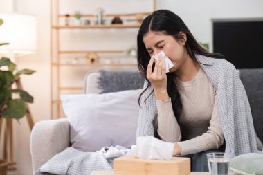 Genç bir kadın kanepeye oturur, battaniyeye sarınır, mendil kullanır, kendini kötü hisseder ve soğuk algınlığıyla ya da grip belirtileriyle savaşır..