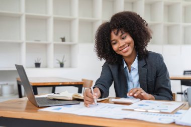 Modern ofis ortamında, masasında özenle mali belgeler üzerinde çalışan bir kadın muhasebeci profesyonellik ve odaklanma gösteriyor..