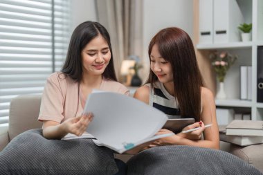 İki genç bayan arkadaş birlikte oturur, çevrimiçi çalışır ve rahat bir ev ortamında ödevlerini yapar, işbirlikçi ve eğitici bir atmosferi teşvik eder..