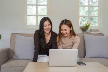 İki gülümseyen kadın, LGBT topluluğunun bir parçası, rahat bir evde dizüstü bilgisayar kullanırken birlikte kanepede vakit geçiriyorlar..