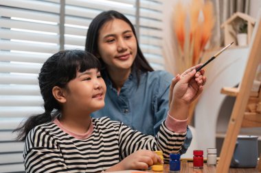 Bir anne ve kızı resim yaparken ve çizerken neşeli bir anı paylaşıyor, yaratıcılığı teşvik ediyor ve evdeki sanat aktiviteleriyle bağ kuruyor..