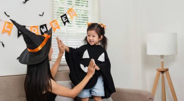 Cadılar Bayramı 'nın tadını çıkaran bir anne ve kızın oturma odalarını şenlikli süslemelerle süslediği iç açıcı bir sahne..