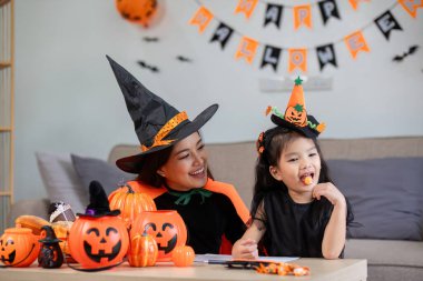 Cadılar Bayramı kostümü giymiş bir anne ve çocuğu, şenlikli süslemeler ve balkabaklarıyla çevrili evde eğlenceli aktivitelere girişiyor..