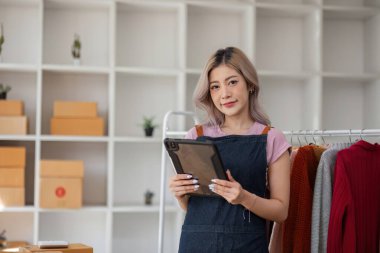 Genç bayan girişimci dijital tablet kullanarak modern ve şık bir çalışma alanında online giyim sektörünü yönetiyor..