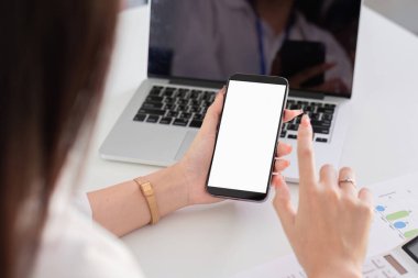 Modern bir ofis ortamında dizüstü bilgisayar üzerinde çalışırken akıllı telefon kullanan genç bir muhasebeci..