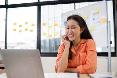 Modern ofis ortamında dizüstü bilgisayarda finansal belgeler üzerinde çalışan genç bir muhasebeci. Arka plandaki cam duvarda yapışkan notlar var..