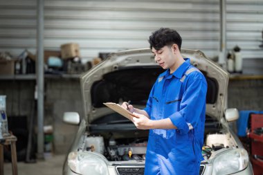 Mavi tulumlu genç bir erkek tamirci araba tamirhanesinde araba bakımı ve profesyonel otomotiv servisine odaklanıyor..