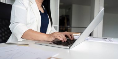 Modern ofis ortamında dizüstü bilgisayarda yazı yazan orta yaşlı bir iş kadını. Masasında bir kalem ve belgeler var..