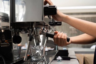 Çağdaş bir kafe ortamında espresso makinesiyle kahve yapan genç bir barista profesyonel barista becerileri sergiliyor..