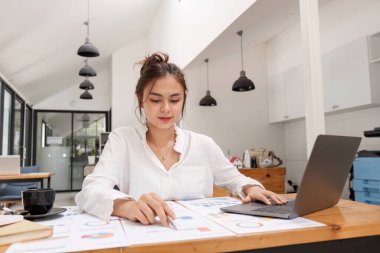Modern bir ofiste finansal belgeler üzerinde çalışan profesyonel kadın muhasebeci, dizüstü bilgisayar kullanıyor ve çizelgeleri analiz ediyor..
