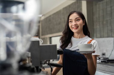 Modern bir kafede genç bir barista, gülümsüyor ve bir fincan kahve tutuyor, profesyonel kahve hazırlama becerileri sergiliyor..