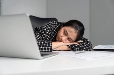 Yorgun ofis çalışanı, masa başında dinleniyor. Etrafı dizüstü bilgisayar ve belgelerle çevrili. İş yerindeki yorgunluk ve yorgunluğu gösteriyor..