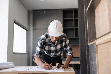 Genç bir mühendis çalışmalarını özgüvenle planlıyor, modern ofis ortamının planlarını inceliyor, profesyonellik ve kendini adamışlık sergiliyor..