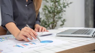 Finansal muhasebe üzerinde çalışan genç bir kadın muhasebeci modern bir ofis masasında dizüstü bilgisayar ve belgelerle veri ve çizelgeleri analiz ediyor..