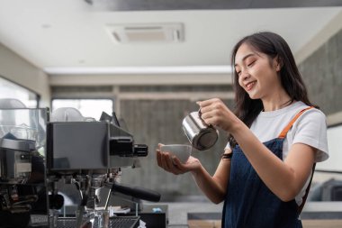Modern bir kafede kahve yapan, gülümseyen ve bir fincana süt döken, profesyonel kahve hazırlama becerileri sergileyen güzel bir barista..