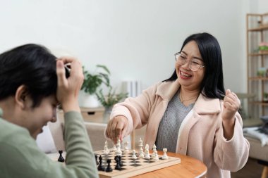 Neşeli bir anne ve oğlu birlikte oturuyorlar, rahat, modern bir oturma odasında satranç oynuyorlar, kaliteli zaman geçiriyorlar ve oyun boyunca birbirlerine bağlanıyorlar..