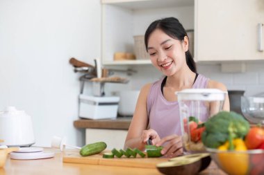 Sağlıklı genç bir kadın taze sebze ve meyvelerle çevrili modern bir mutfakta taze meyve suyu yapıyor..