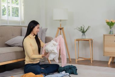 Giysileri bavula katlayan, yolculuğa hazırlanan hoş bir kadın. Yüzünde bir gülümsemeyle, rahat, modern bir oturma odasında yerde oturuyor..