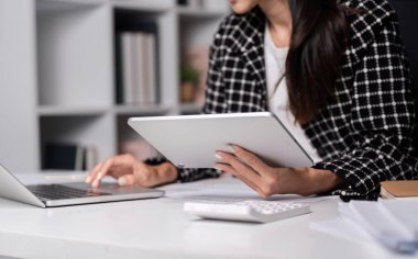 Çağdaş bir ofis ortamında tablet ve dizüstü bilgisayardaki mali verileri analiz eden profesyonel bir iş kadını.