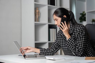 İş kadını, ofis masasında geç saatlere kadar çalışırken kendini stresli ve bitkin hissediyor. Dizüstü bilgisayar ve telefonda birden fazla iş yapıyor..