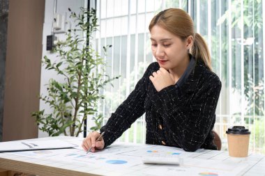 Ofis masasında, elinde kahve fincanı ve hesap makinesiyle haritalar ve grafiklerle özenle çalışan profesyonel bir iş kadını..