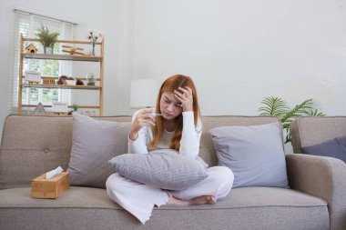 Kanepede oturan genç bir kadın termometreyle ateşini ölçüyor ve sağlığı için endişeleniyor..