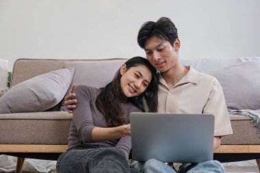 Genç bir çift kanepede birlikte rahatlar, dizüstü bilgisayarlarını paylaşır ve rahat, modern bir oturma odasında kaliteli zaman geçirirler..