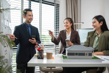 Emlakçılar modern bir ofiste pazarlama planlarını tartışıyor, emlak sektöründe takım çalışması ve strateji geliştirme sergiliyorlar..