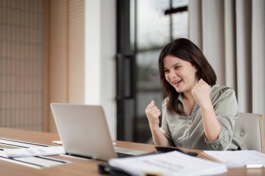 Neşeli bir iş kadını, modern ofis ortamında heyecan ve mutluluğu ifade ederek başarılı bir iş başarısını kutluyor..