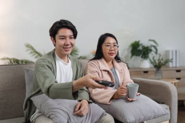 Bir anne ve oğlu, modern bir oturma odasında televizyon izleyip rahat bir kanepede kaliteli vakit geçiriyorlar..