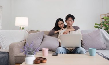 Bir çift rahat bir koltukta dinleniyor, modern bir oturma odasında dizüstü bilgisayar paylaşıyor, birlikte kaliteli zaman geçiriyorlar..