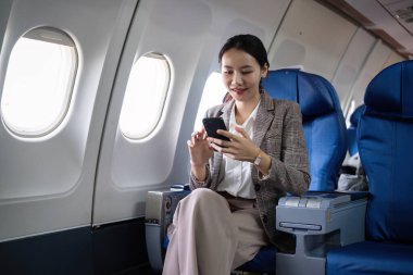 Uçakta seyahat ederken telefonunu kullanan genç bir iş kadını. Modern bir uçak kabininde profesyonel bir bayan yolcu..
