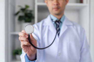 Beyaz önlüklü, elinde steteskop tutan kendine güvenen bir erkek doktor. Modern bir muayenehanede profesyonelliği ve uzmanlığı simgeliyor..