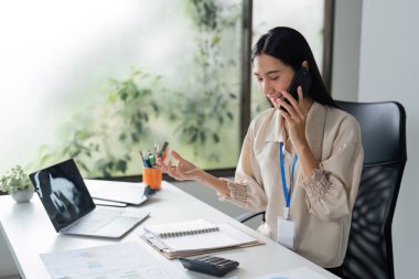 Parlak, modern ofis ortamında telefon ve dizüstü bilgisayarla çalışan profesyonel bir iş kadını..