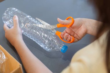 Genç kadın plastik şişeleri geri dönüşümle kullanışlı ev eşyalarına dönüştürmek, sürdürülebilirliği ve çevre dostu yaşamı desteklemek için yaratıcı bir şekilde kesiyor..