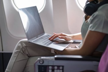 Genç bir kadın internette çalışmak için laptopunu kullanıyor. Odaklanmış, üretken, modern seyahat ve teknolojiyi gözler önüne seriyor..