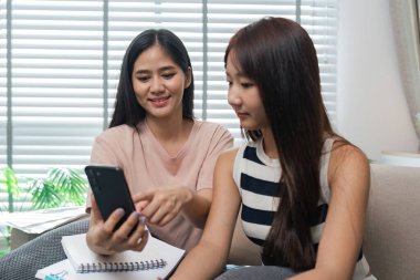 Birlikte okuyan ve online sınavlara giren iki genç kadın samimi, modern bir ev ortamında dostluk ve işbirliği sergiliyorlar..