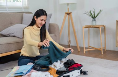 Neşeli genç bir kadın bavulunu rahat, modern bir oturma odasında hazırlar. Tatile ya da geziye sevinç ve heyecanla hazırlanır..