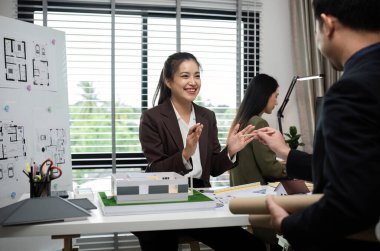 Mimari planlar ve modern ofis ortamında bir modelin yer aldığı bir emlak projesi hakkında bir tartışma içine giren bir iş dünyası profesyonelleri ekibi.