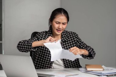 Ofis malzemeleri ve dizüstü bilgisayarla çevrili masasında kağıt yırtarak hayal kırıklığını ifade eden bir iş kadını..